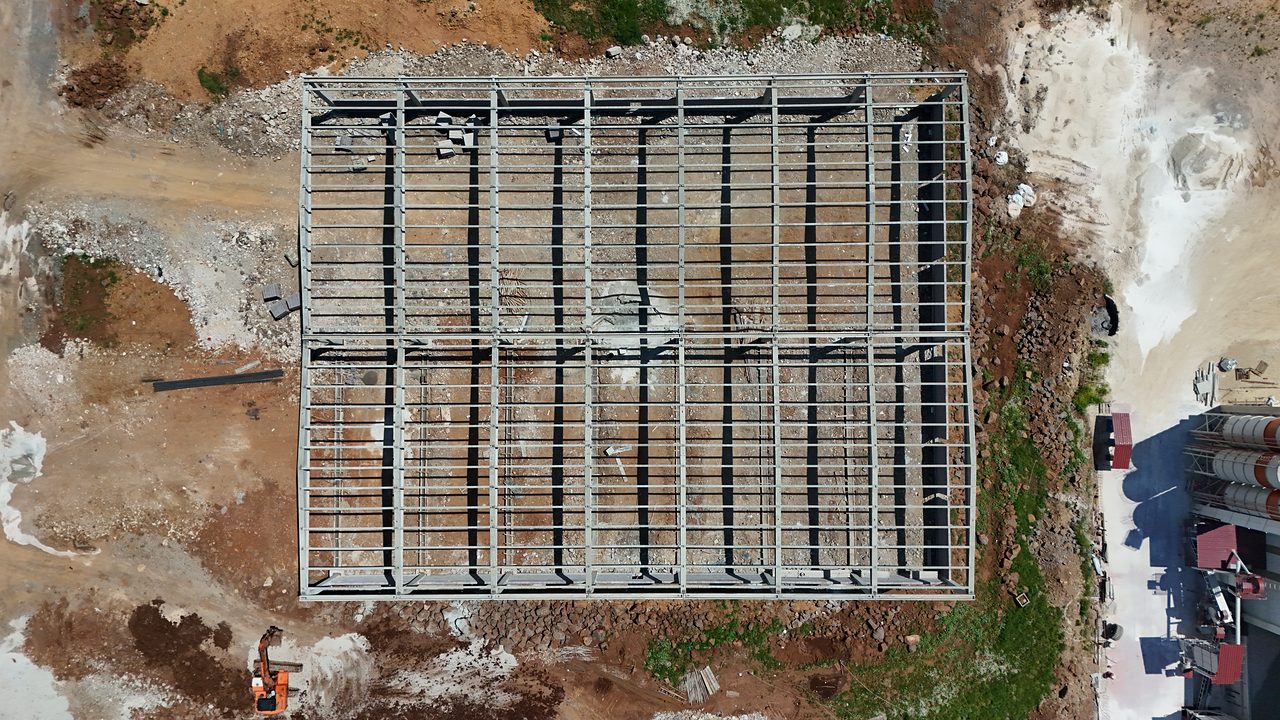 Top-down shot showing the grid of the precast frame and the rhythm of the roof purlins.