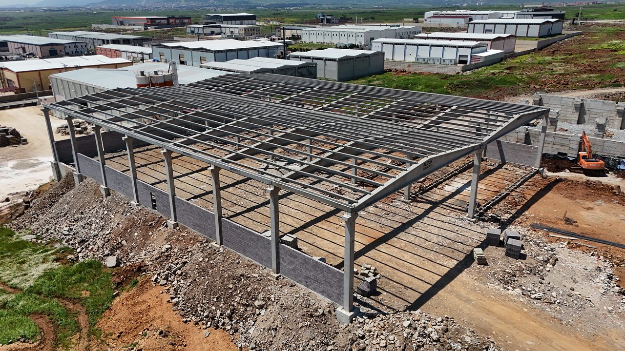 Precast concrete frame for a food production plant in İslahiye: columns, roof girders and purlins, with the industrial zone and mountains behind.