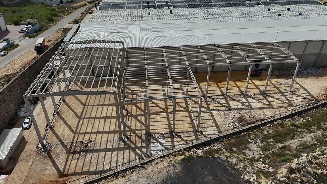 Mevcut fabrika binasının yanında montajı süren prefabrik ek yapı: kolonlar ve çatı iskeleti.