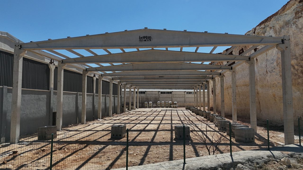 Long precast frame of columns, roof girders and purlins running along a cut slope.