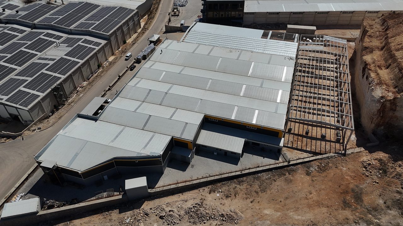 Precast expansion rising next to an existing factory, with roof cladding under way.