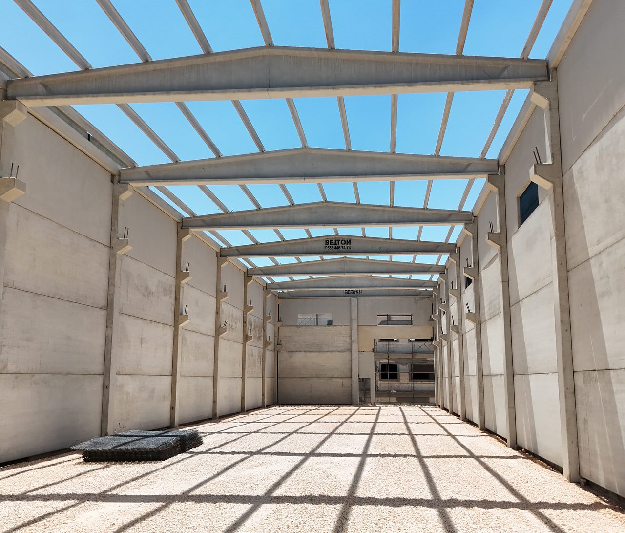 Symmetrical hall interior: precast wall panels on both sides, girders above and purlin shadows on the floor.