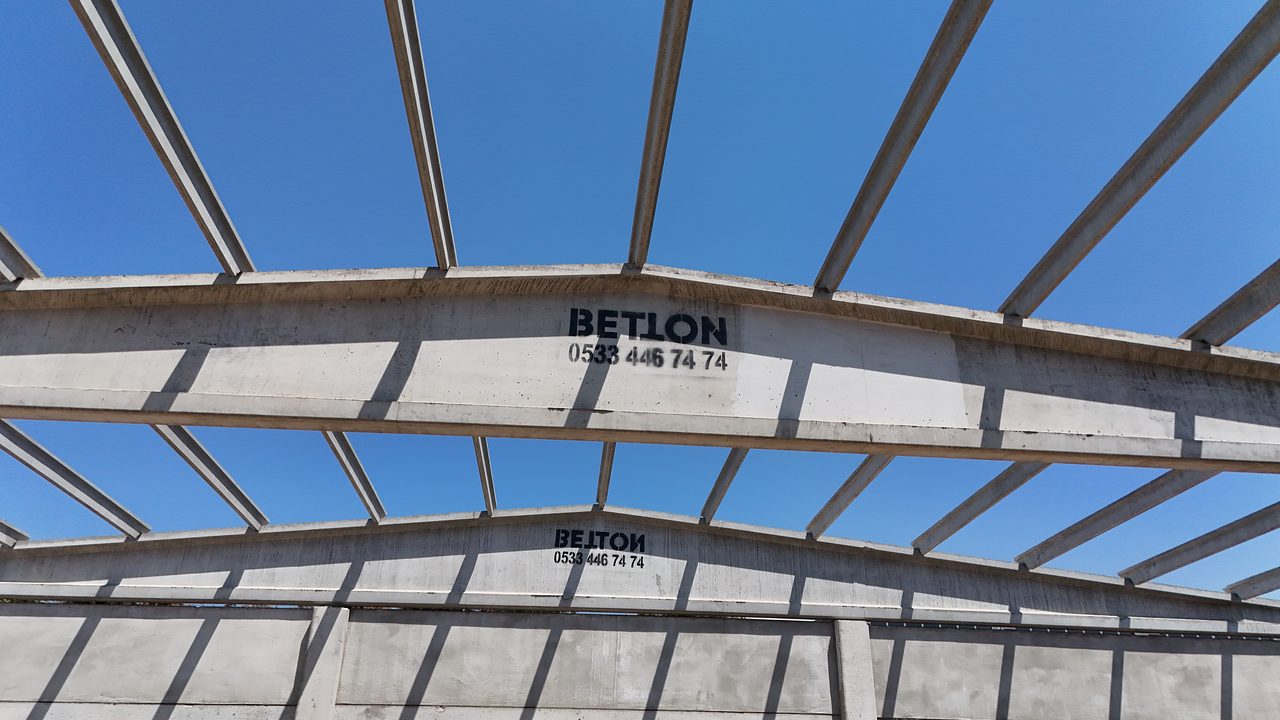 Two prestressed roof girders stamped BETTON against a blue sky, with purlins resting on them.