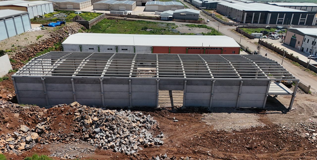 Precast industrial building in İslahiye: a long hall with wall panels and a completed roof frame, surrounded by the industrial zone.